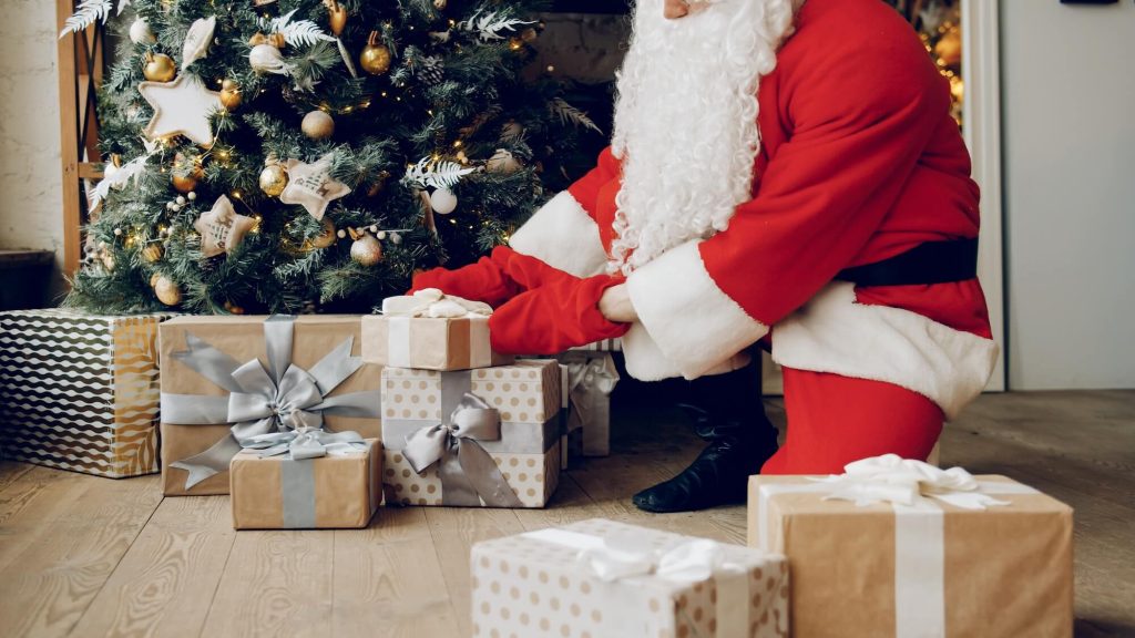 Santa laying gifts under a decorated tree.